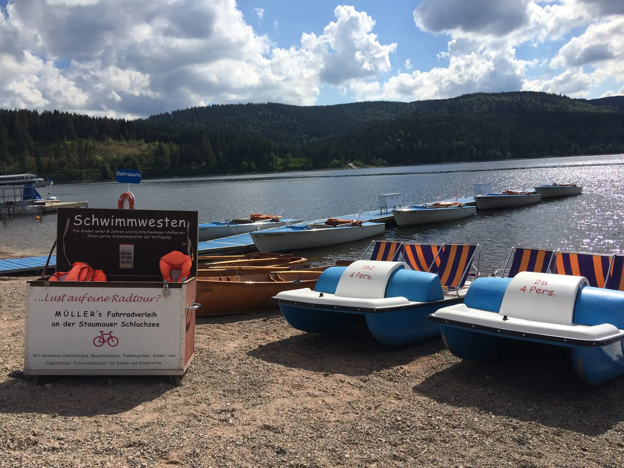 Weiter Blick über den Schluchsee mit Booten am Ufer und den Bergen des Schwarzwalds